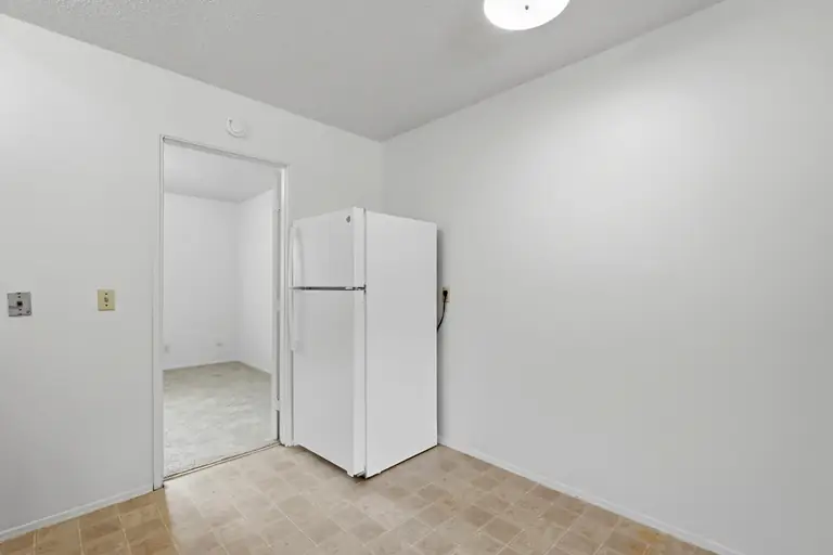 Kitchen area with the refrigerator and a doorway to the bedroom