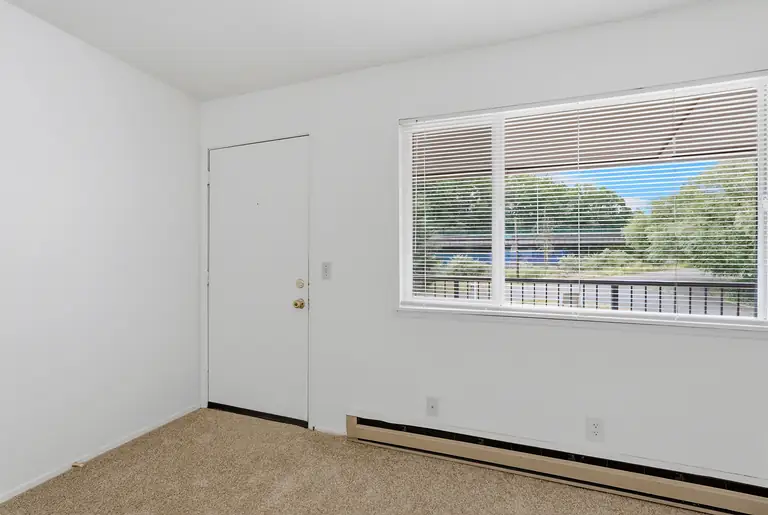 Living room with front door, large window with blinds and baseboard heater